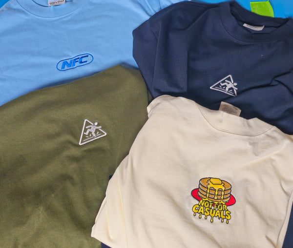 Multiple embroidered designs on Shaka Wear Max tees for Not For Casuals
